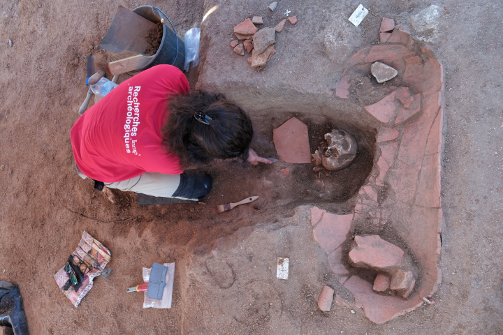 Une archéologue de l’Inrap est en train de fouiller une sépulture médiévale en pleine terre ayant recoupée une sépulture en amphore africaine antérieure.