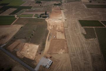 Vue aérienne depuis le nord-est du décapage du site du Péras. On distingue les trois secteurs de fouille : Péras 2, au premier plan à gauche, et les deux autres, qui constituent  Péras 1, en haut de l'image de part et d'autre d'un chemin orienté nord-ouest/sud-est. Le Péras, Mauguio (Hérault), 2013. © Archéodrone, Inrap