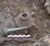 Balsamaire en verre et biberon en terre cuite déposés dans une fosse funéraire.